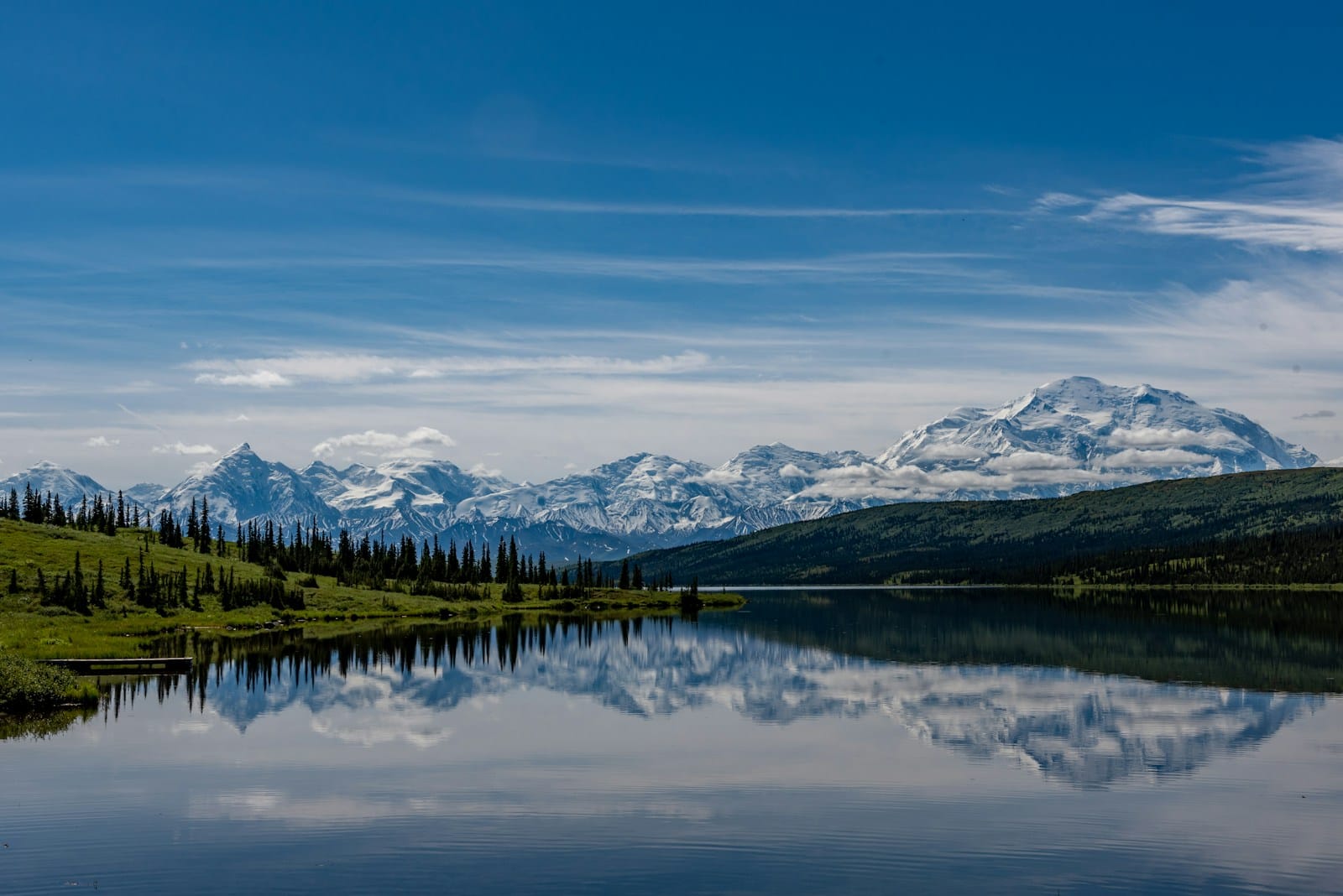 Alaska Travel Guide green trees near lake under blue sky during daytime