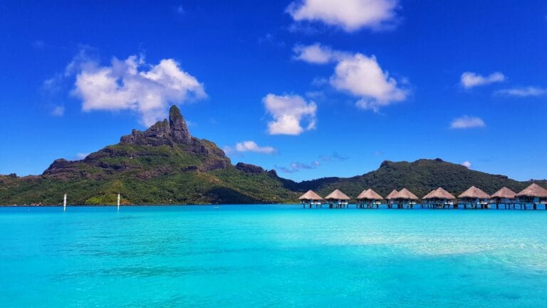 Blue Waters green mountain beside body of water under blue sky during daytime