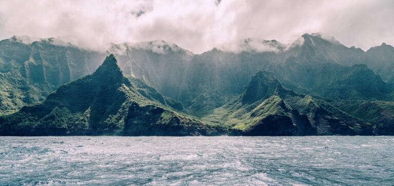 Kauai Travel Guide body of water near mountain under cloudy sky during daytime