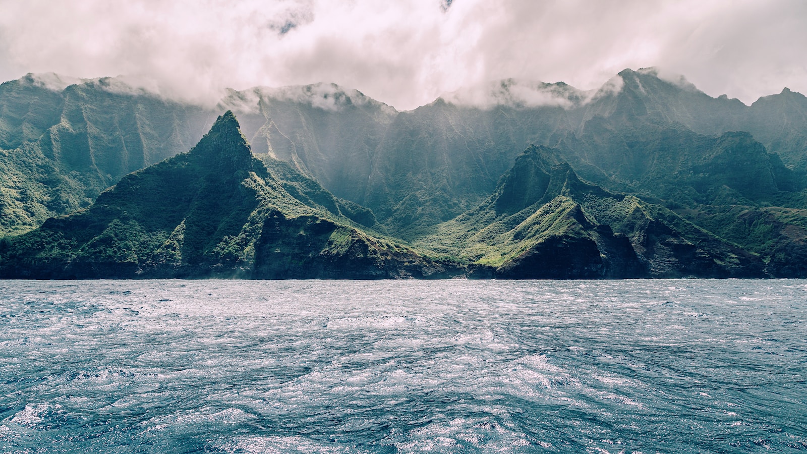 Kauai Travel Guide body of water near mountain under cloudy sky during daytime