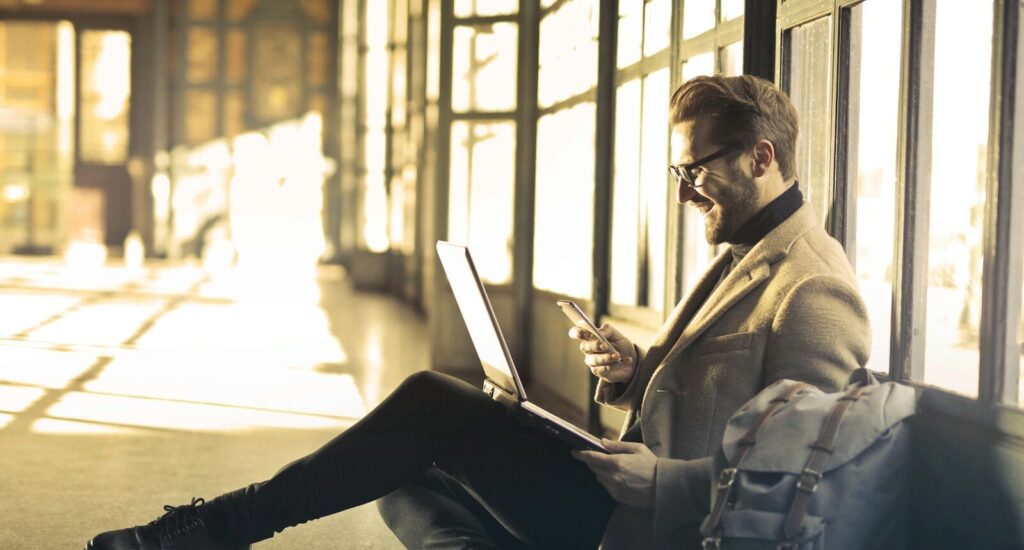 Airalo man sitting near window holding phone and laptop