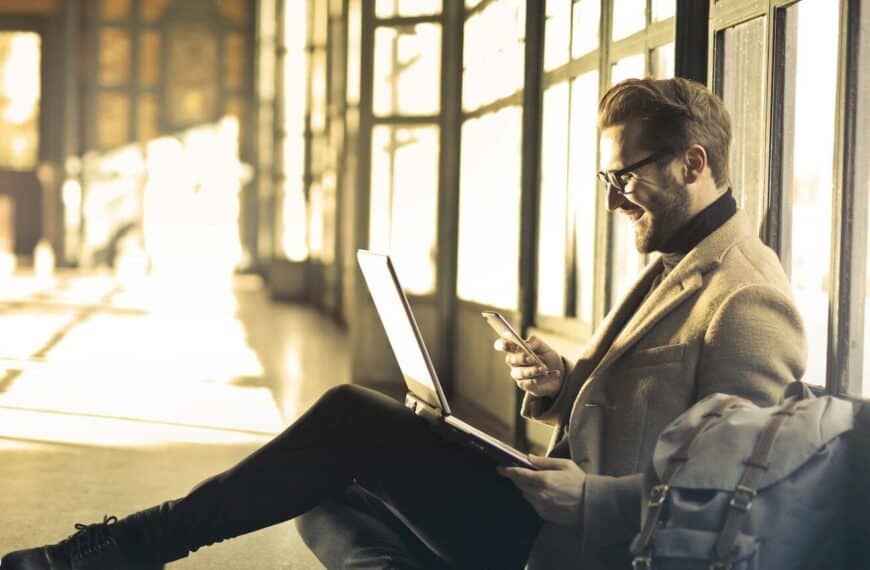 Airalo man sitting near window holding phone and laptop