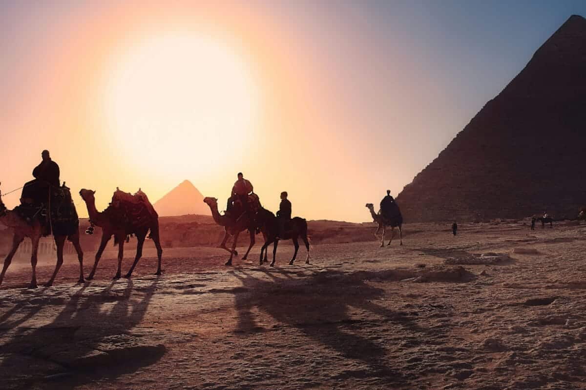 Egypt Tours five persons riding camels walking on sand beside Pyramid of Egypt