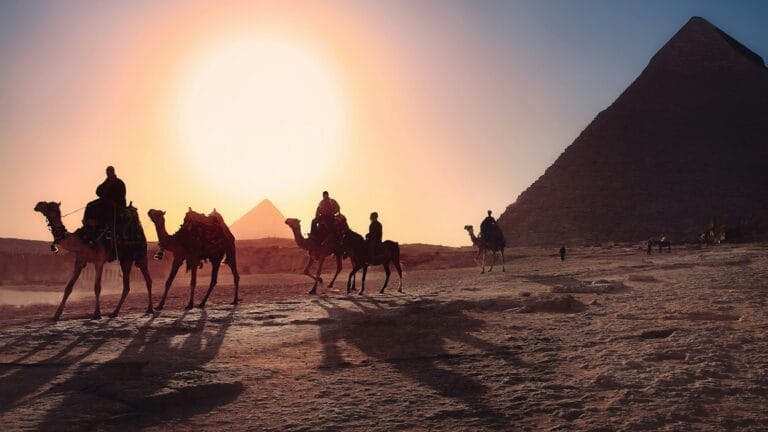 Egypt Tours five persons riding camels walking on sand beside Pyramid of Egypt