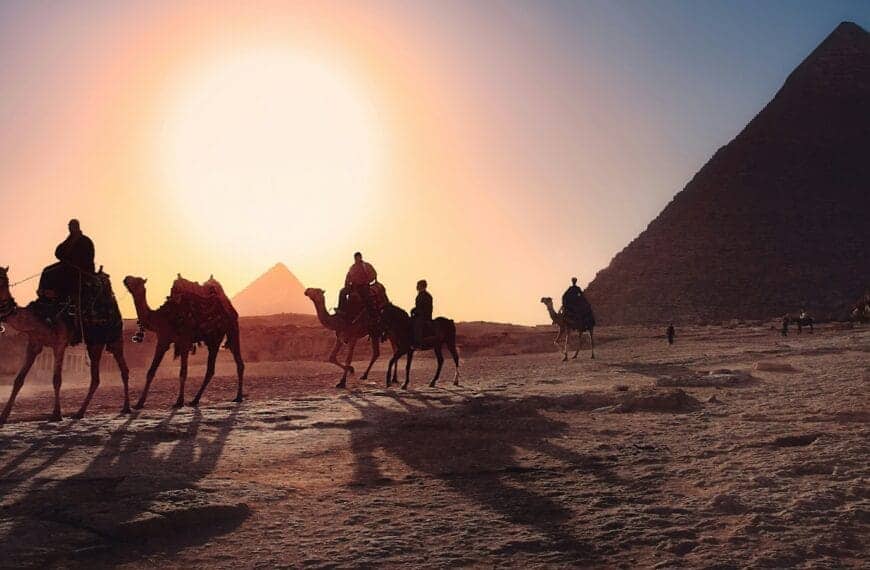 Egypt Tours five persons riding camels walking on sand beside Pyramid of Egypt