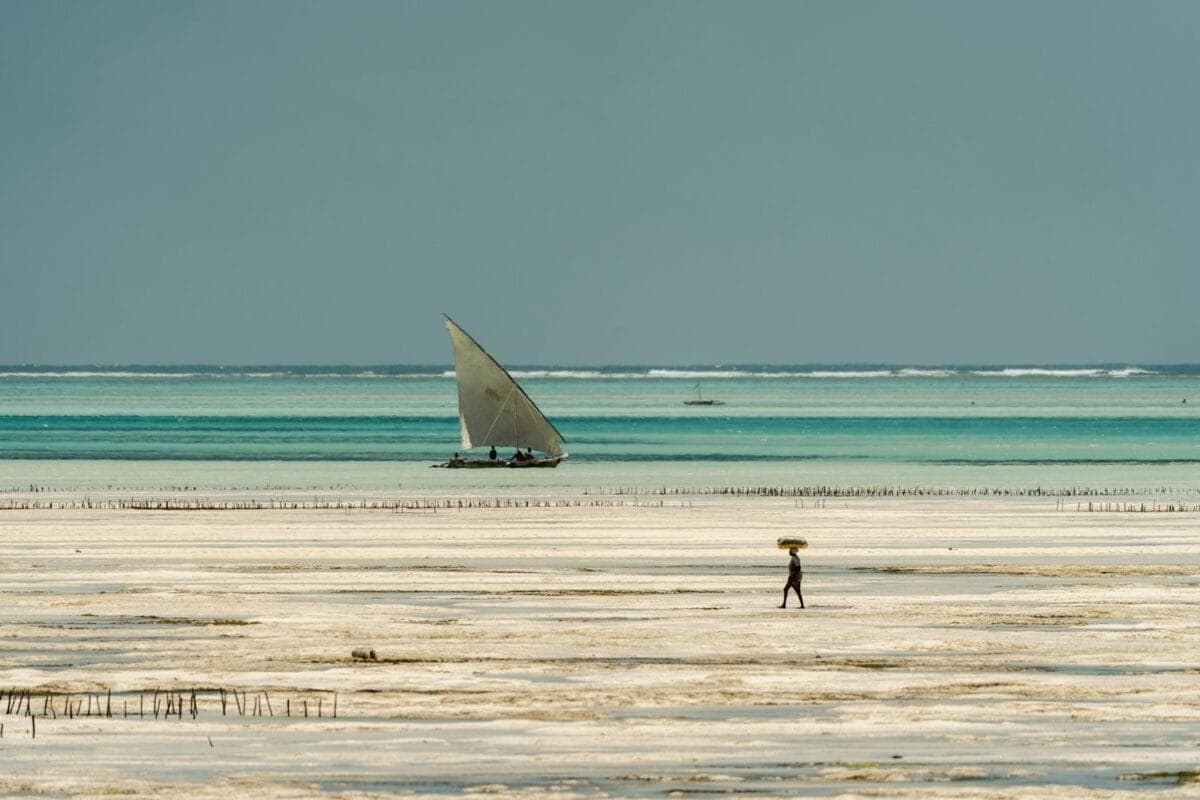 East Africa Travel Guide a person standing on a beach with a sailboat in the background