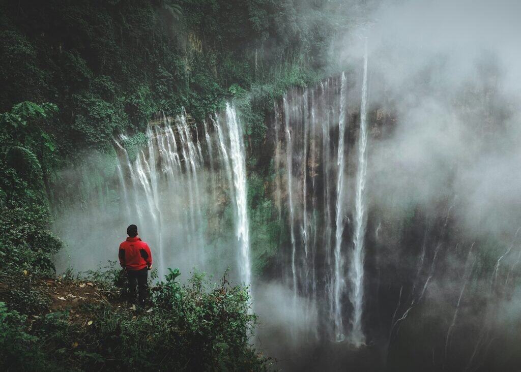 Wanderlust Travel Guide man standing on cliff facing waterfall
