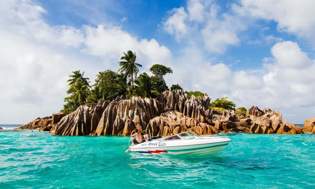 Seychelles Tours white and blue boat on sea near green palm trees during daytime
