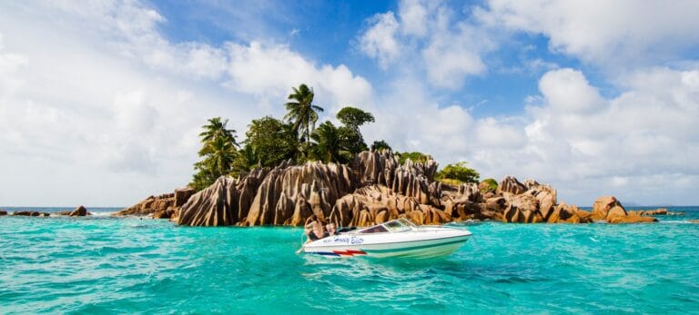Seychelles Tours white and blue boat on sea near green palm trees during daytime