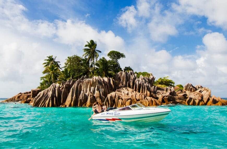Seychelles Tours white and blue boat on sea near green palm trees during daytime
