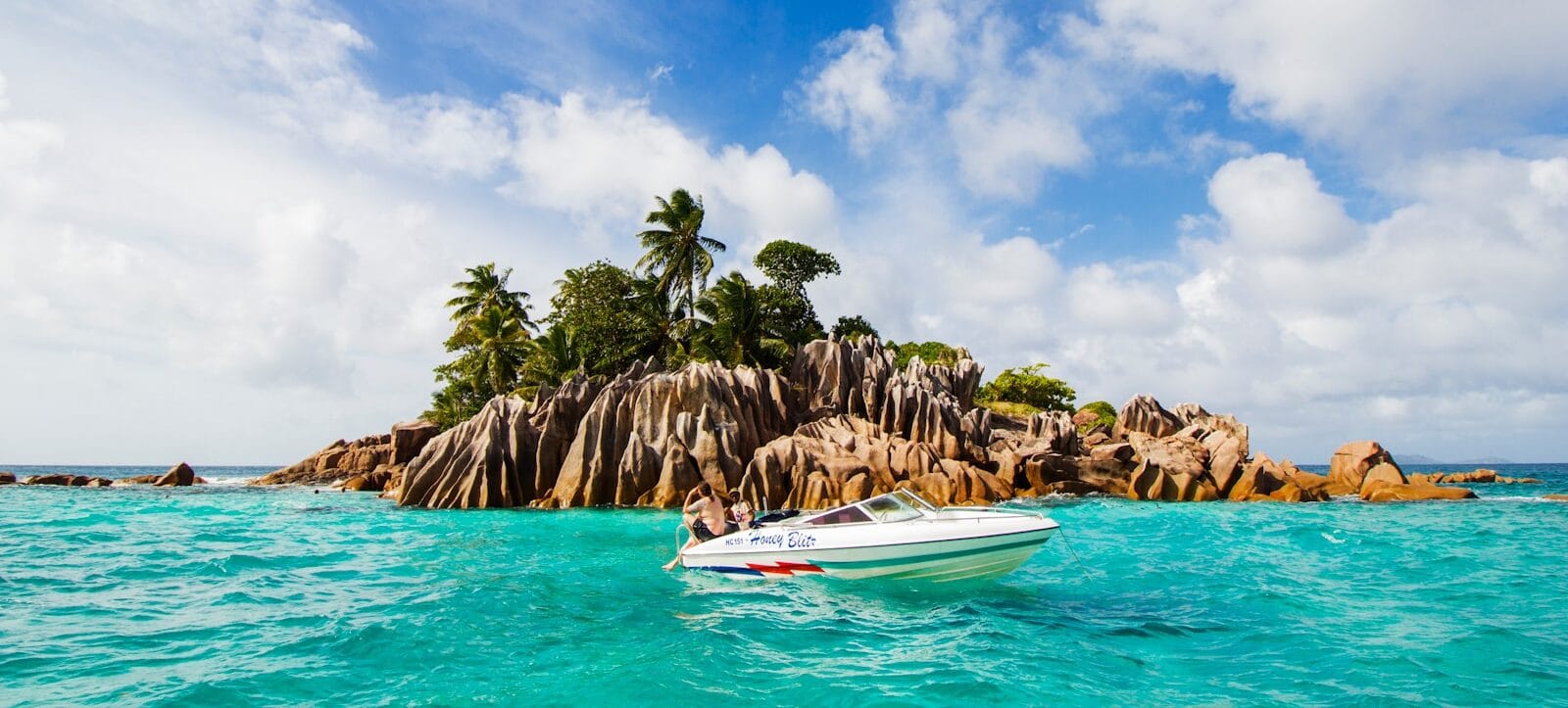 Seychelles Tours white and blue boat on sea near green palm trees during daytime