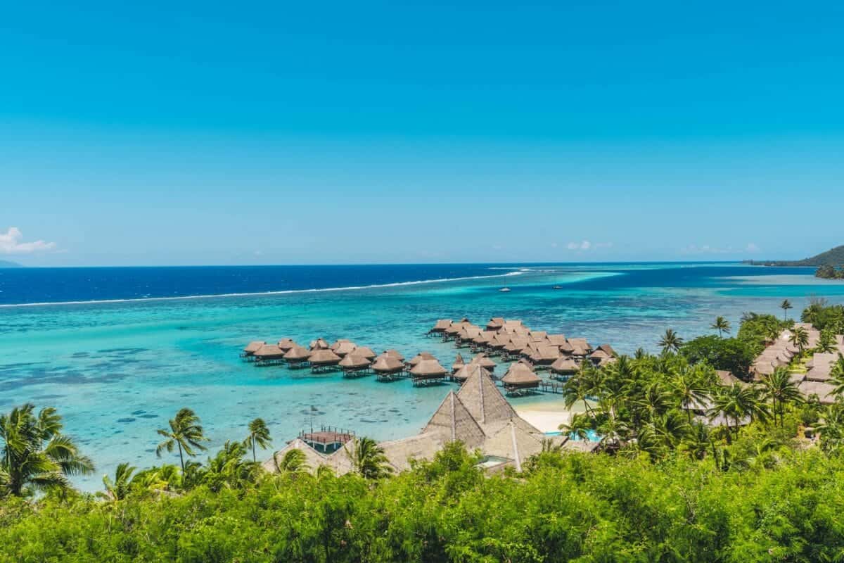moorea tours A tropical beach with thatched huts and blue water