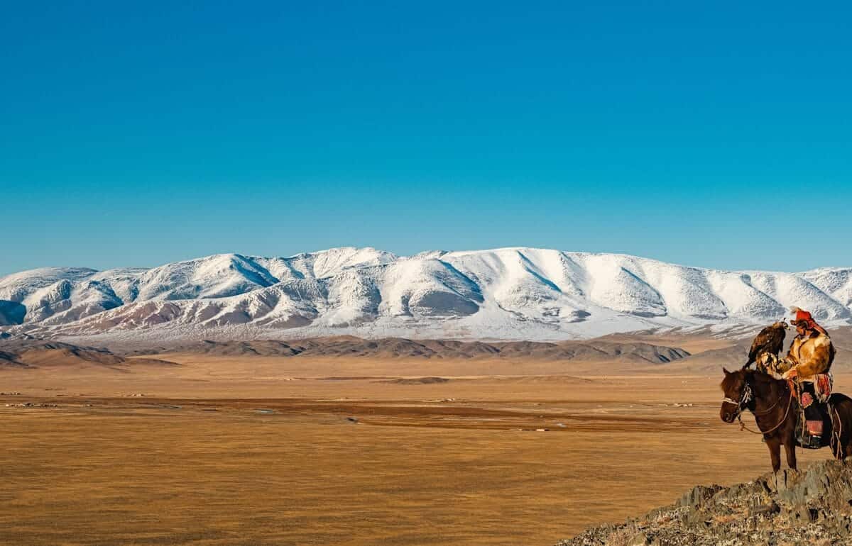 Mongolia Travel Guide Horse rider overlooks snowy mountains and plains.