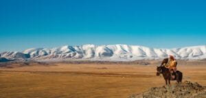 Mongolia Travel Guide Horse rider overlooks snowy mountains and plains.