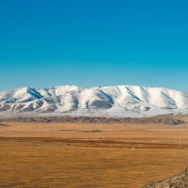 Mongolia Travel Guide Horse rider overlooks snowy mountains and plains.
