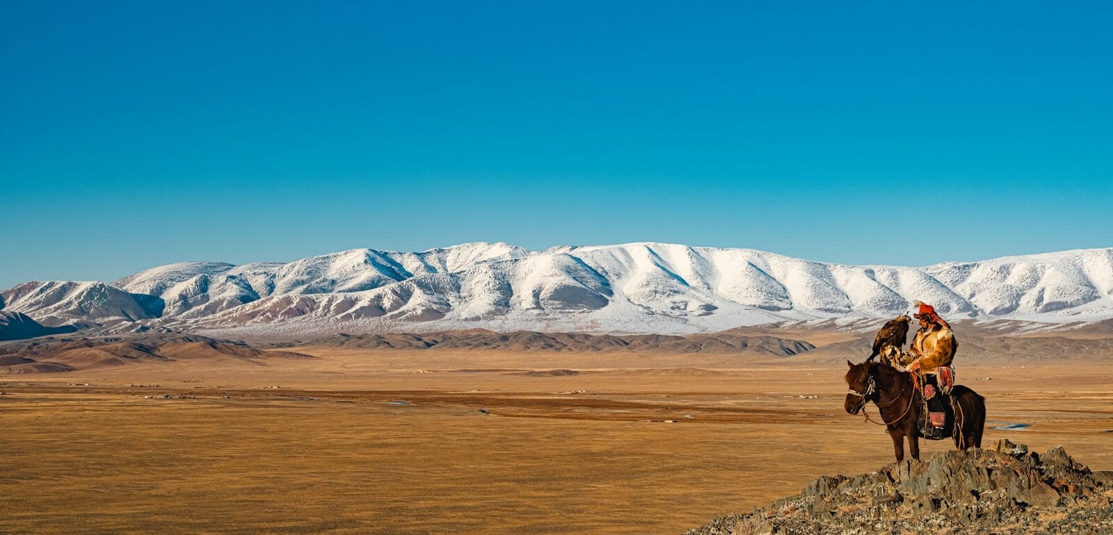 Mongolia Travel Guide Horse rider overlooks snowy mountains and plains.