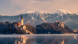 Slovenia travel guide brown and white concrete building near lake and snow covered mountain during daytime