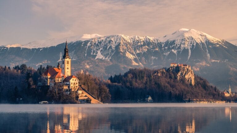 Slovenia travel guide brown and white concrete building near lake and snow covered mountain during daytime