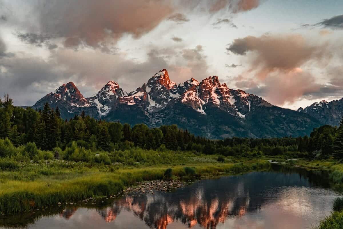 Wyoming Travel Guide green trees near lake and snow covered mountain during daytime