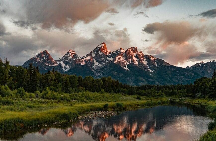 Wyoming Travel Guide green trees near lake and snow covered mountain during daytime