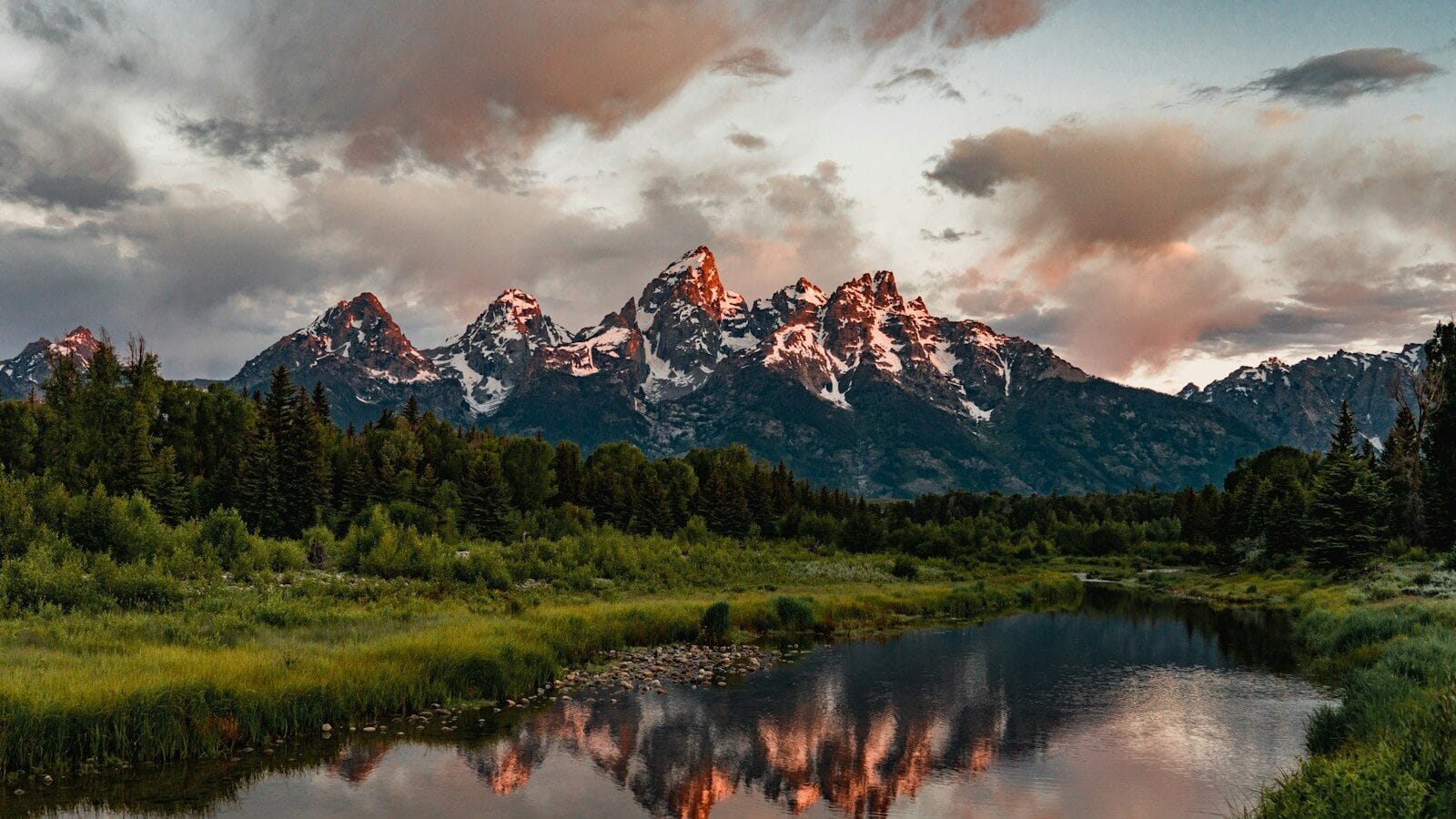 Wyoming Travel Guide green trees near lake and snow covered mountain during daytime