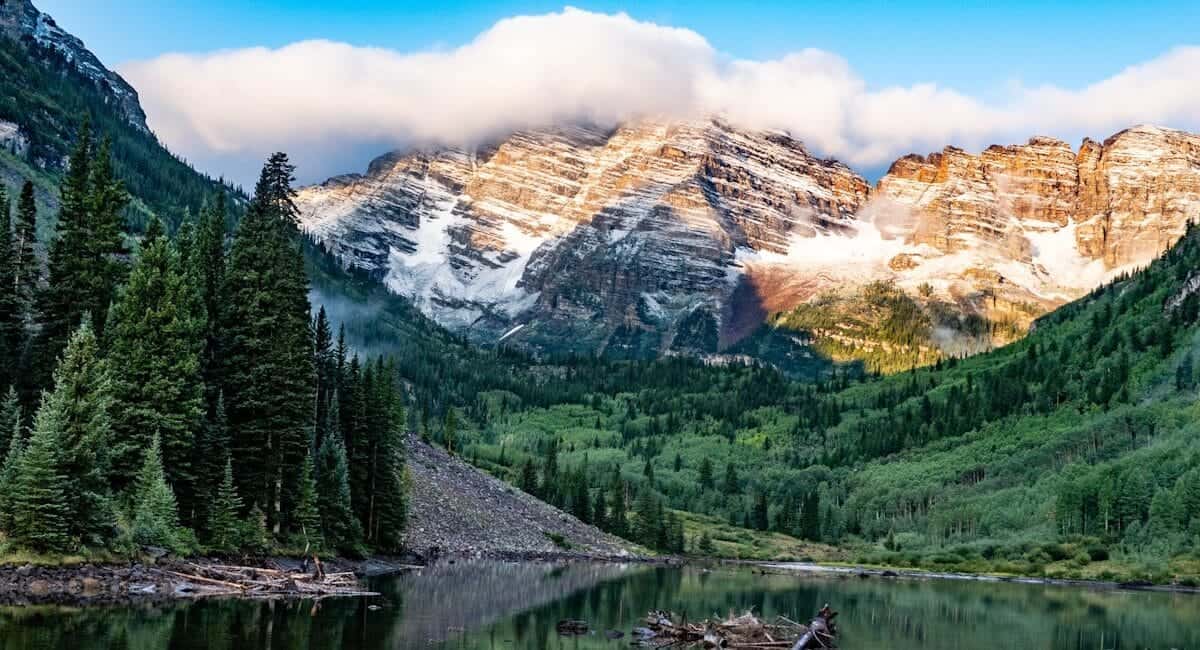 Colorado Travel Guide green pine trees near lake and snow covered mountain during daytime