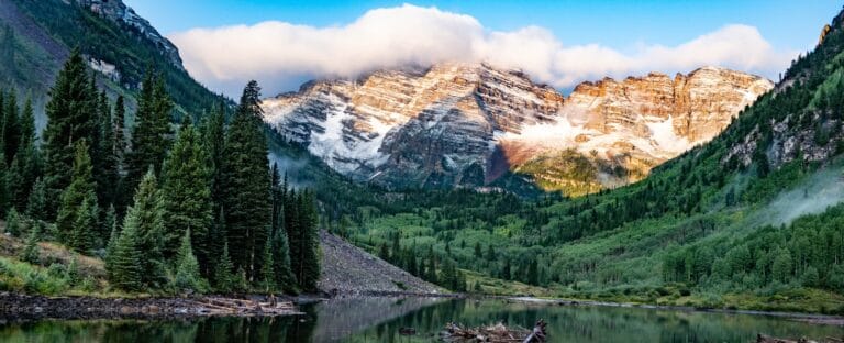 Colorado Travel Guide green pine trees near lake and snow covered mountain during daytime