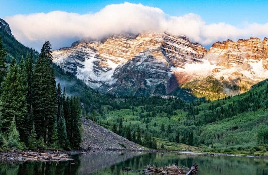 Colorado Travel Guide green pine trees near lake and snow covered mountain during daytime