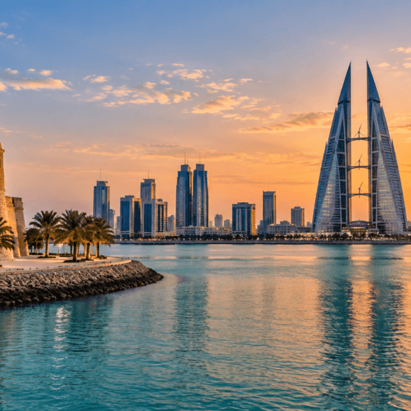Bahrain waterfront at sunset with palm-lined historic architecture and Manama's modern skyline across the water.