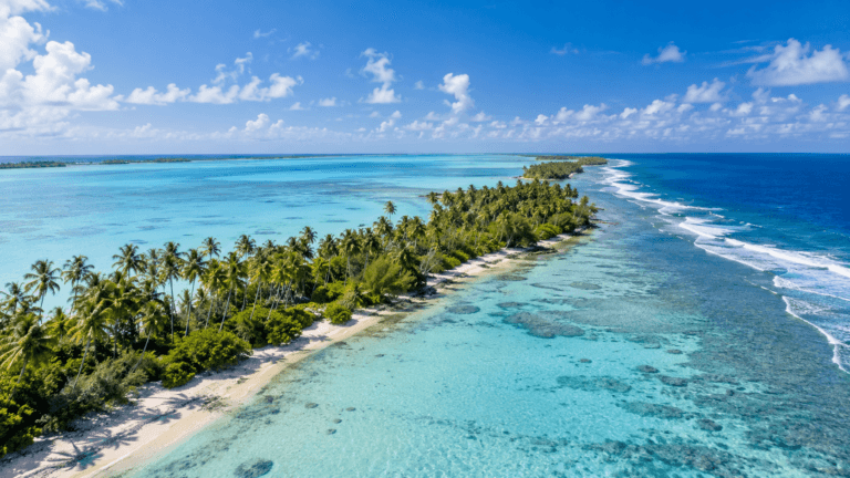 Aerial view of a palm-covered Kiribati atoll bordered by a turquoise lagoon, coral reef, and deep blue Pacific Ocean.