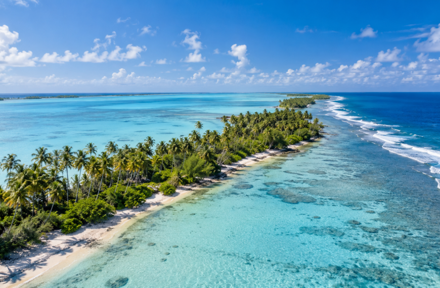Aerial view of a palm-covered Kiribati atoll bordered by a turquoise lagoon, coral reef, and deep blue Pacific Ocean.