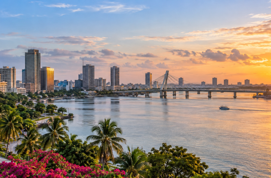 Abidjan skyline, lagoon, cable-stayed bridge, palm-lined waterfront and boat beneath a warm sunset sky in Côte d’Ivoire.