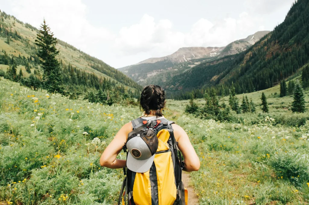 Carry-On Packing Checklist person carrying yellow and black backpack walking between green plants
