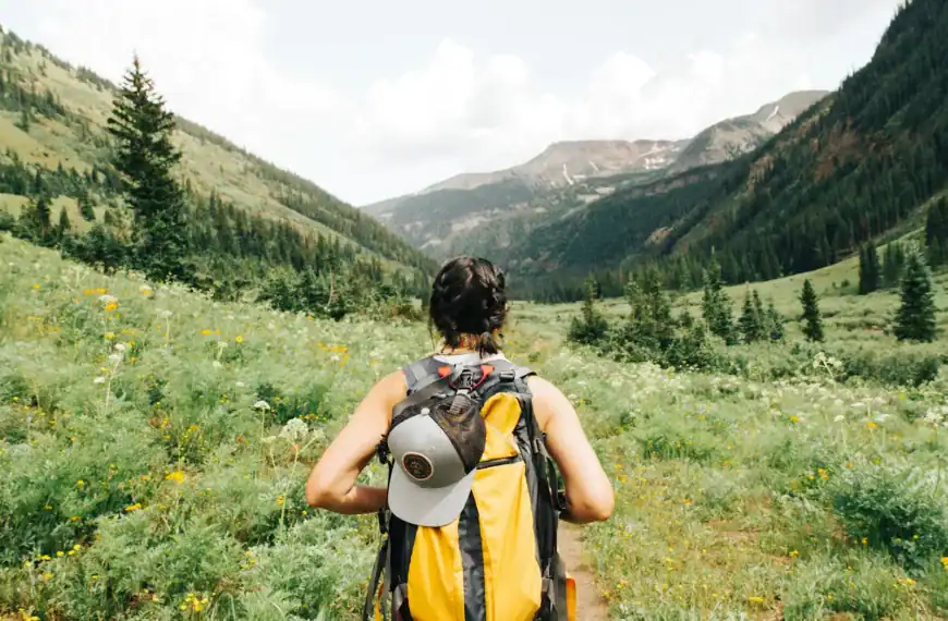 Carry-On Packing Checklist person carrying yellow and black backpack walking between green plants